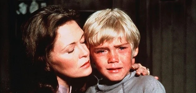 A woman comforts a crying child with blonde hair