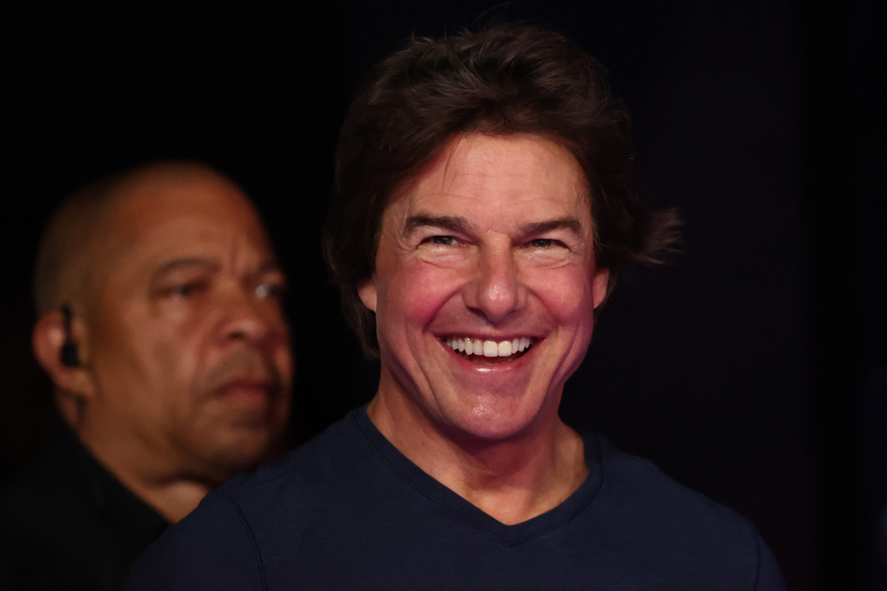 Tom Cruise smiling with a security guard standing behind him