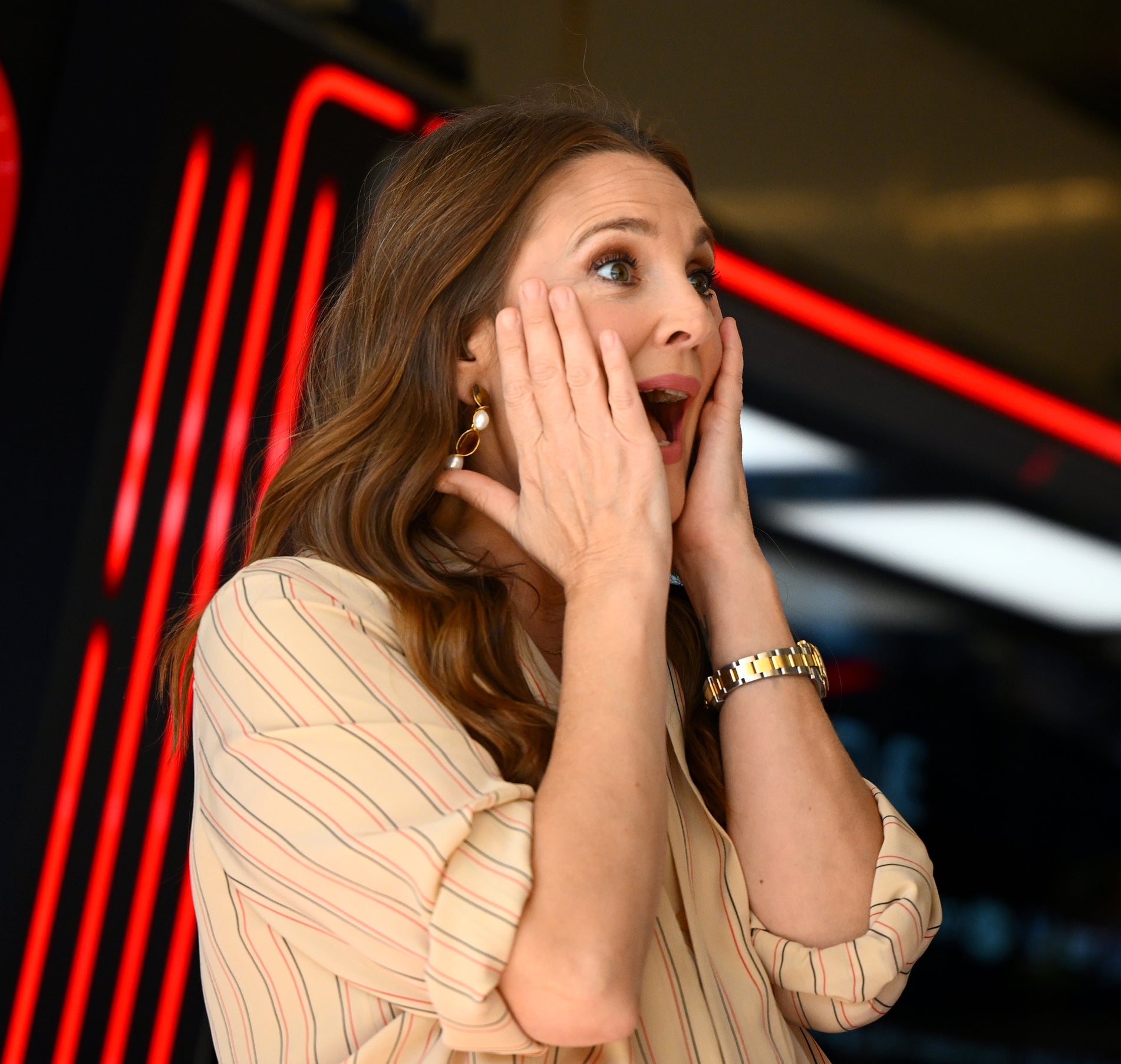 Drew Barrymore looking surprised while chatting with Sergio Pérez, who is in Red Bull Racing uniform