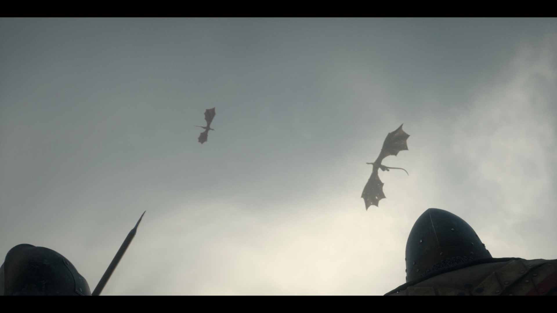 Two knights watch two dragons flying high in the sky, their spears pointing upward