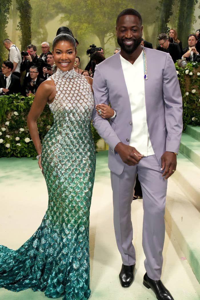 Gabrielle Union in a fitted, mermaid-style gown and Dwyane Wade in a light-colored suit at a public event. They are smiling and posing