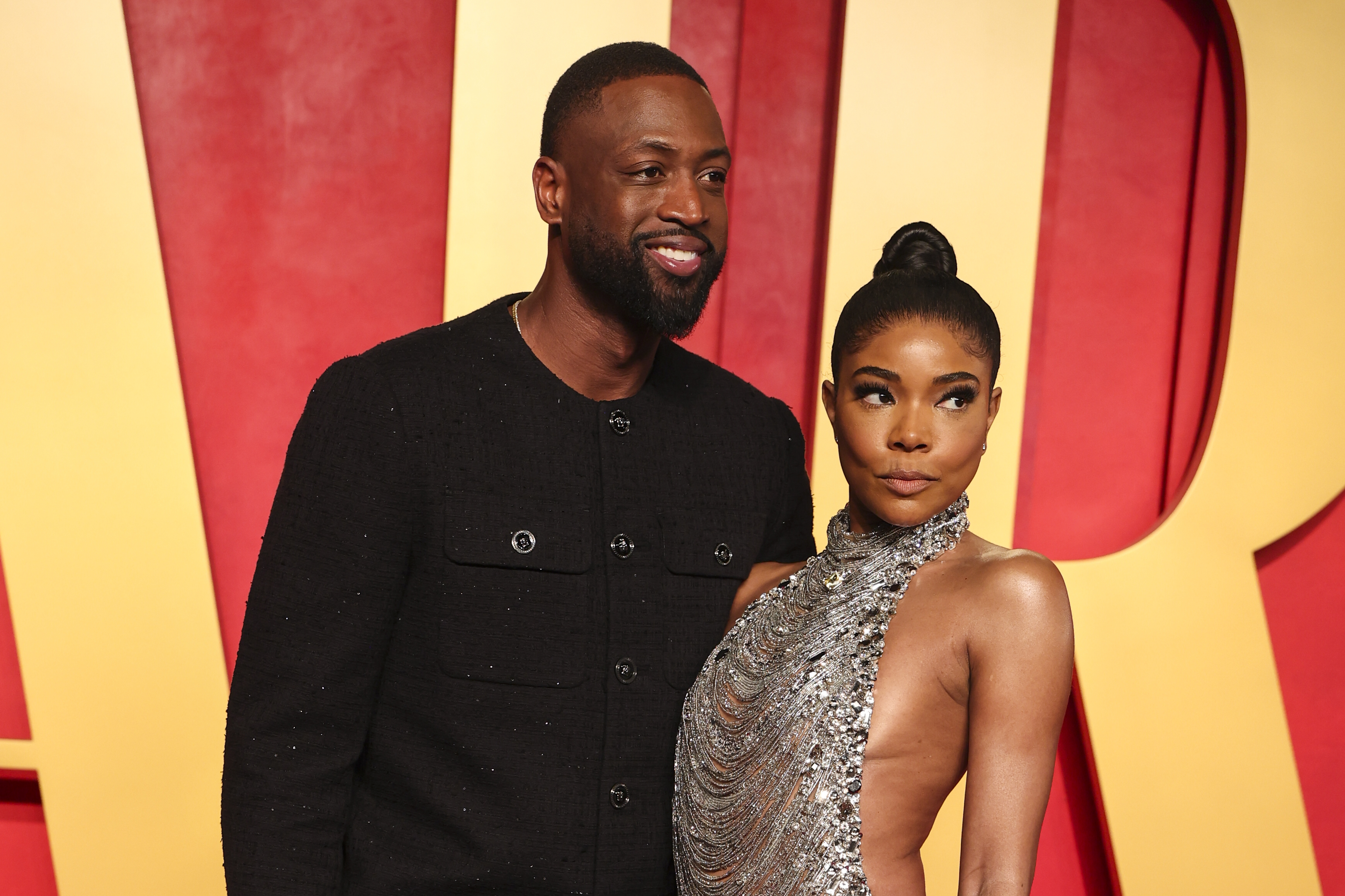 Dwyane Wade and Gabrielle Union pose on the red carpet. Wade wears a black jacket, and Union wears a silver, sequined gown