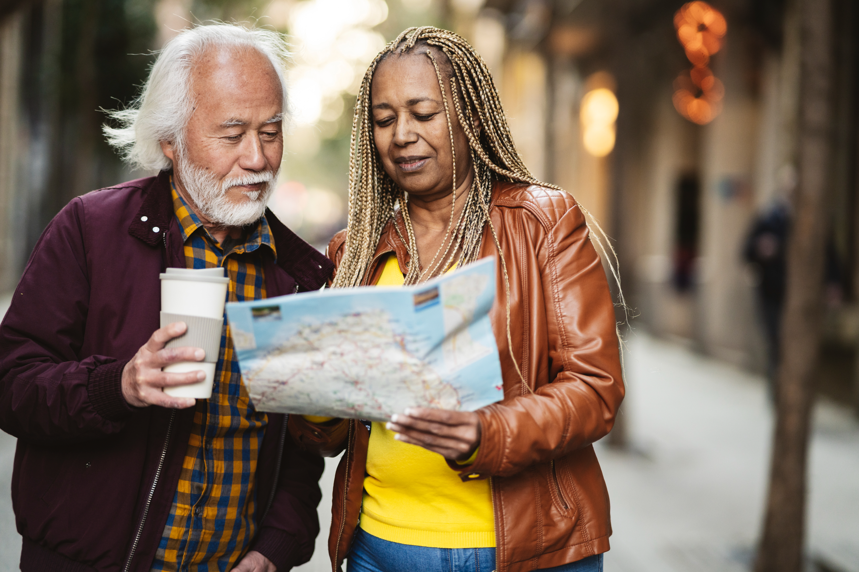 Elderly couple reading a map and holding a coffee cup on a city street