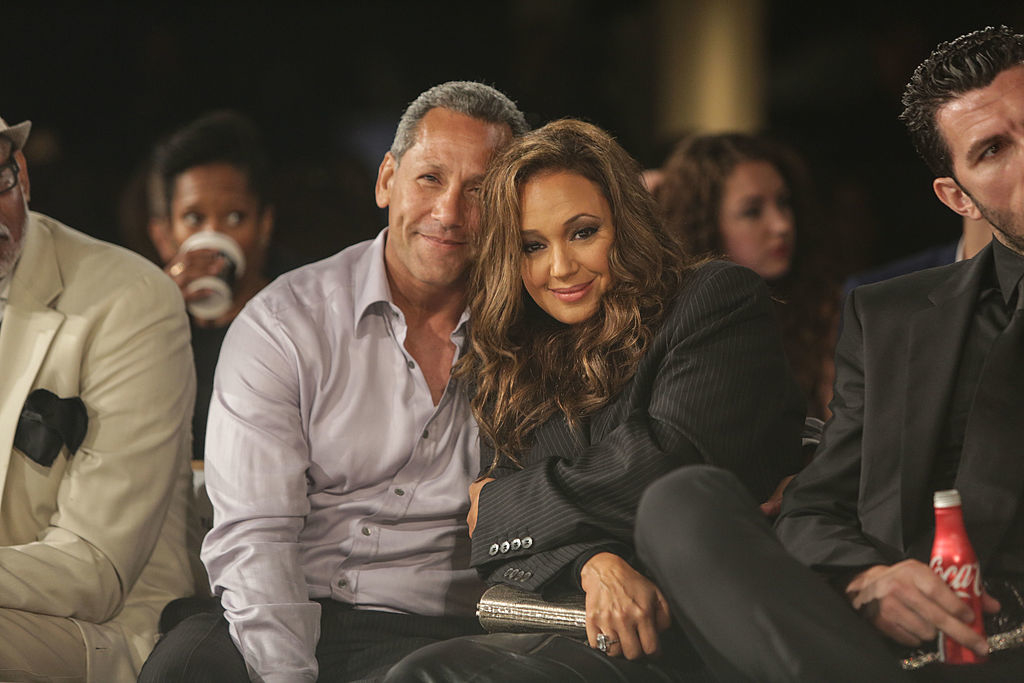A man and Leah Remini, in formal attire, sit closely together, smiling for the camera at an event. Others are also seated around them