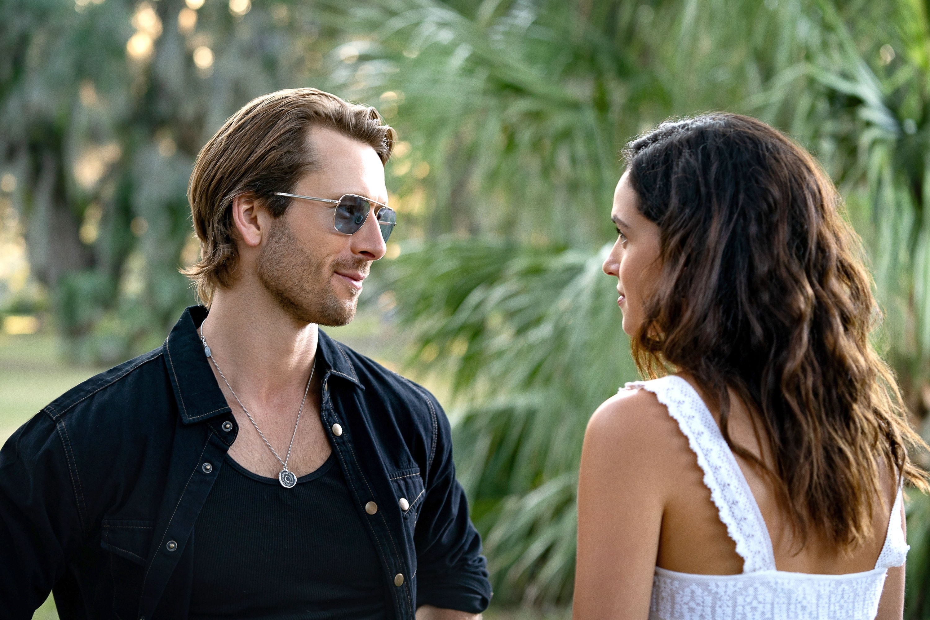 Glen Powell and Adria Arjona in an outdoor scene, casually dressed, facing each other