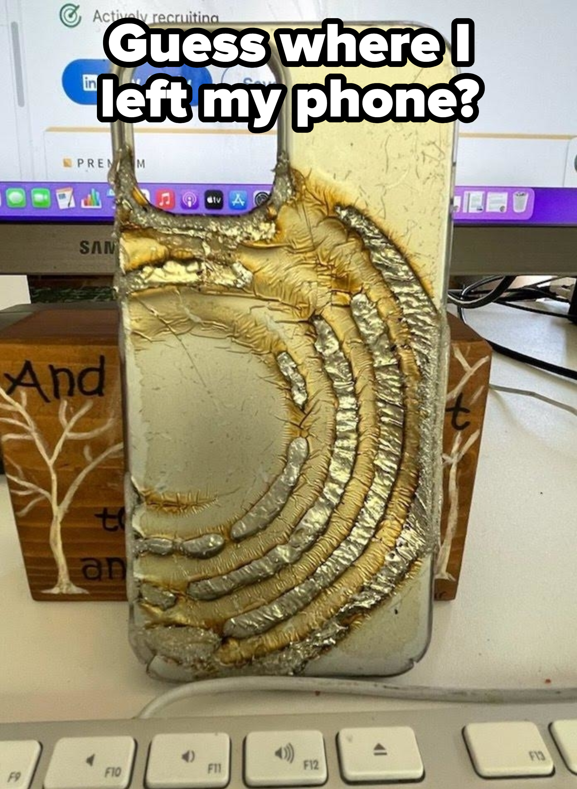 A phone with a severely melted and damaged case on a desk near a keyboard and computer monitor