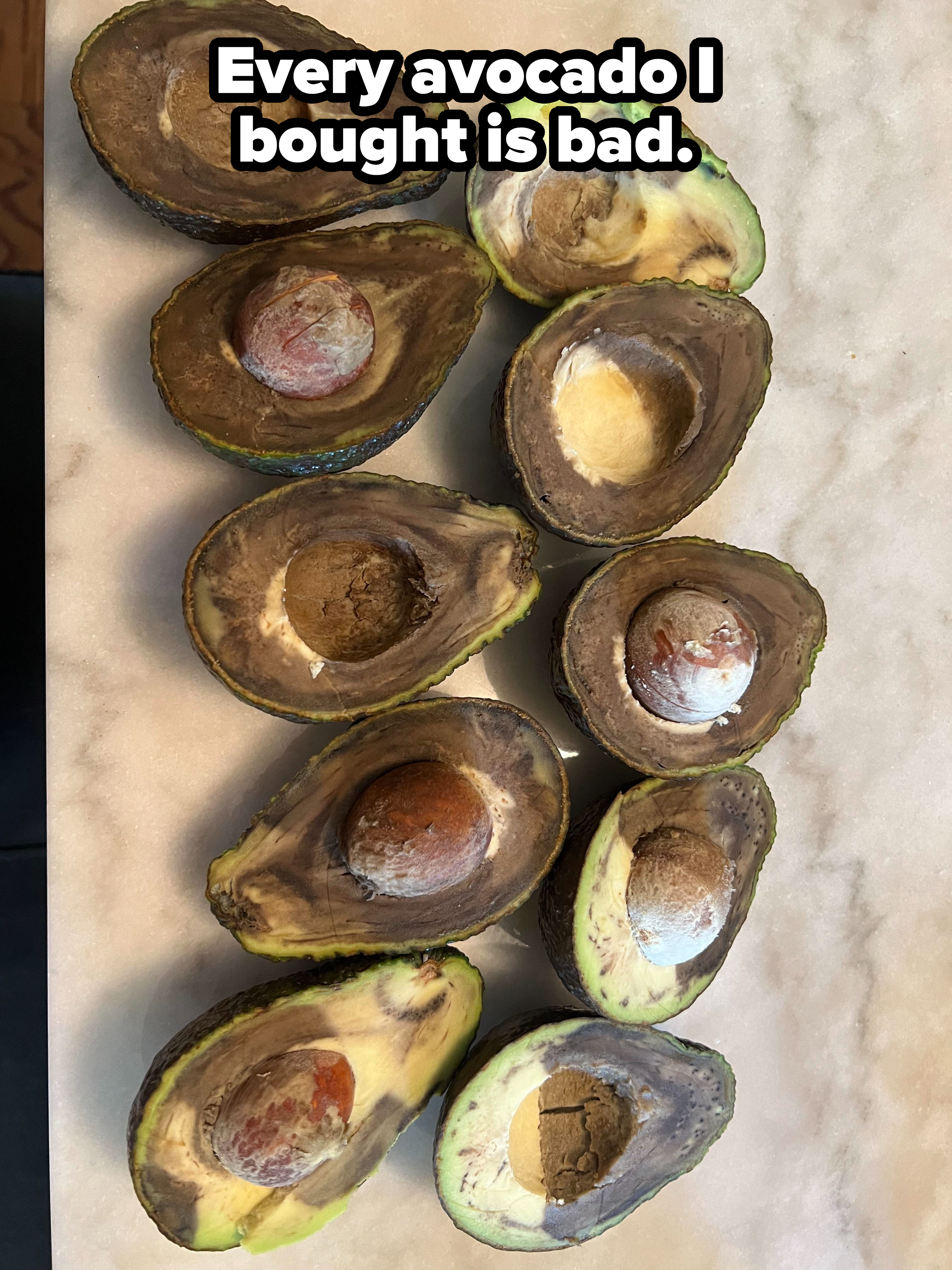 Multiple halves of avocados are shown, most of which are overripe with brown spots and deteriorating flesh on a marble surface