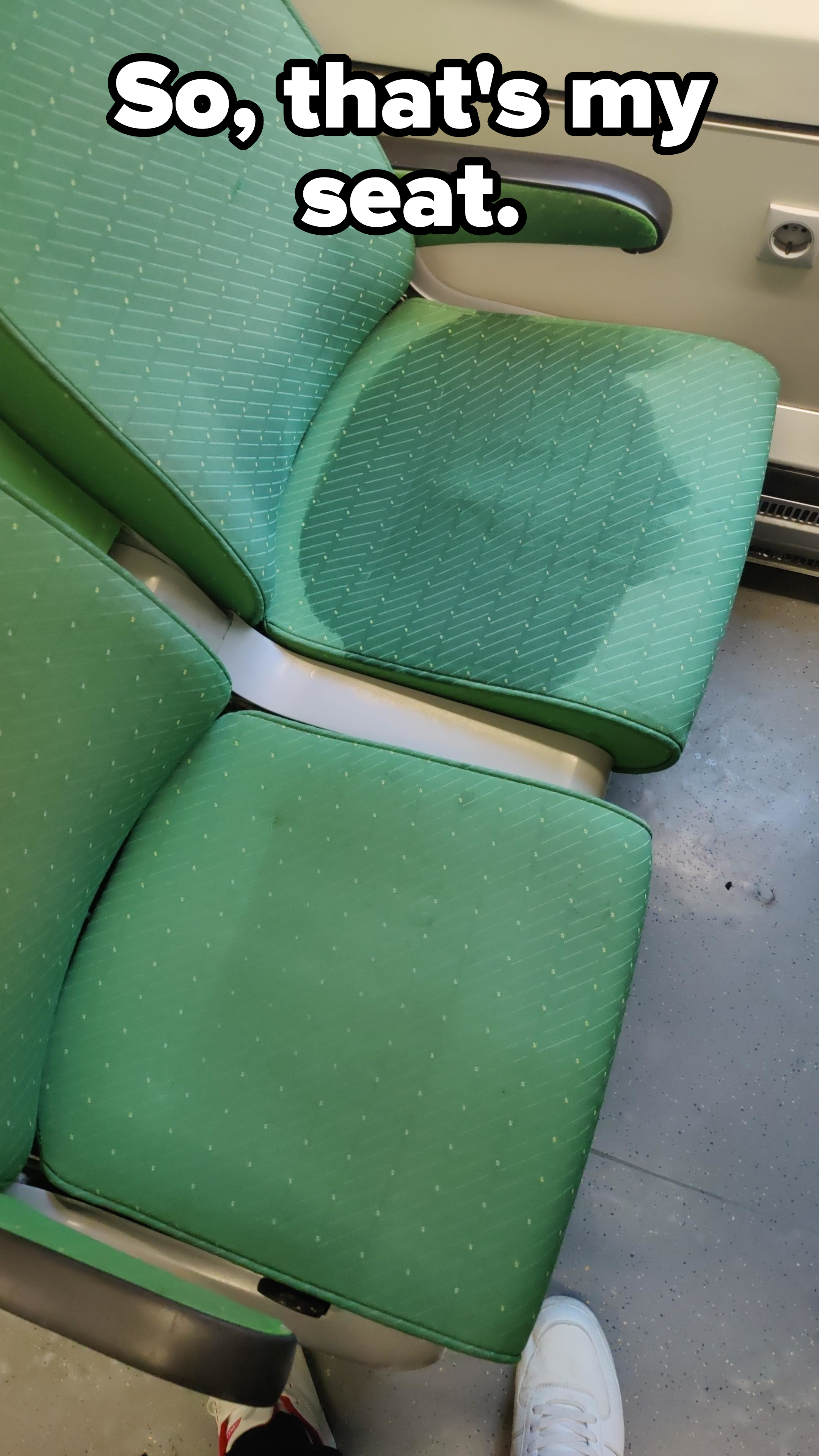 Train seat with a visible wet spot on the right side. The image shows the green padded seats of a train or similar public transit