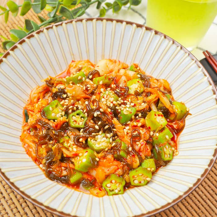 おくらとキムチが盛られたボウルの料理。ゴマのトッピングが見える。テーブルには緑茶の飲み物も置かれている。