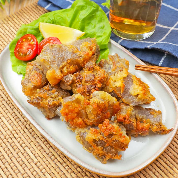 おひたしの皿に盛り付けられた唐揚げ、付け合わせにミニトマトとレモン。隣にビールのグラスとお箸が置かれている。