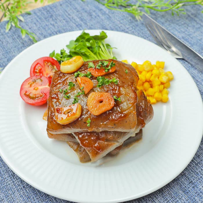 白いプレートに盛られた、トマト、コーン、グリーン野菜と一緒にガーリックソースで味付けされた料理。