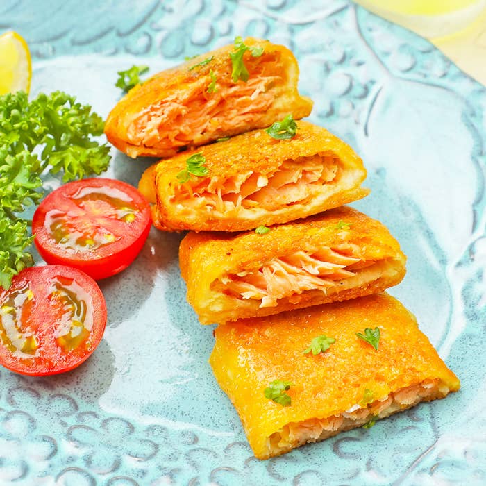 4つの切り身に分けられたサーモンのパイ包み焼きと、輪切りのトマトとパセリのガーニッシュ。