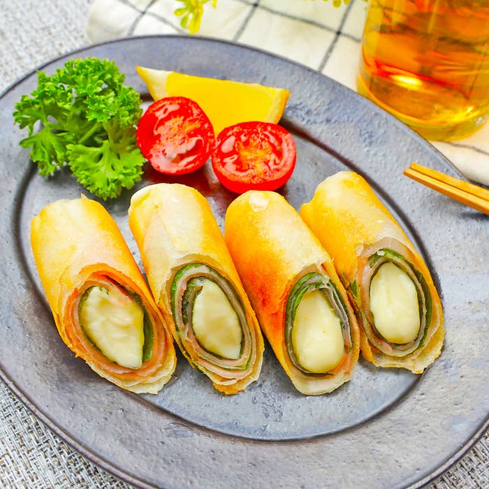 お皿に盛られた4つの春巻き、トマトのスライス、パセリ、レモンが添えられている。隣に飲み物がある。