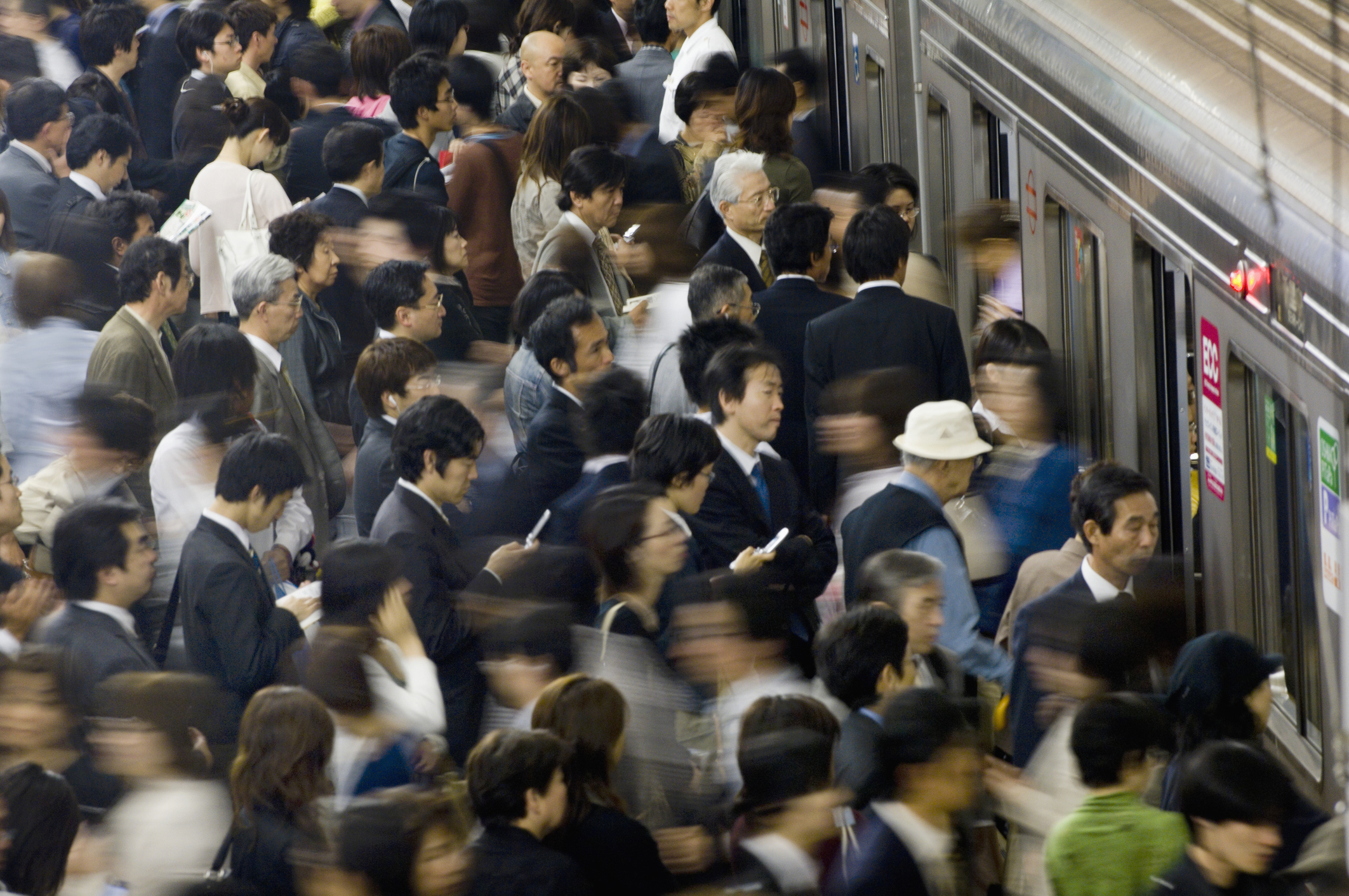 A large crowd of people, mostly in business attire, rush into a subway train during peak hours. The scene captures the bustling atmosphere of the subway station