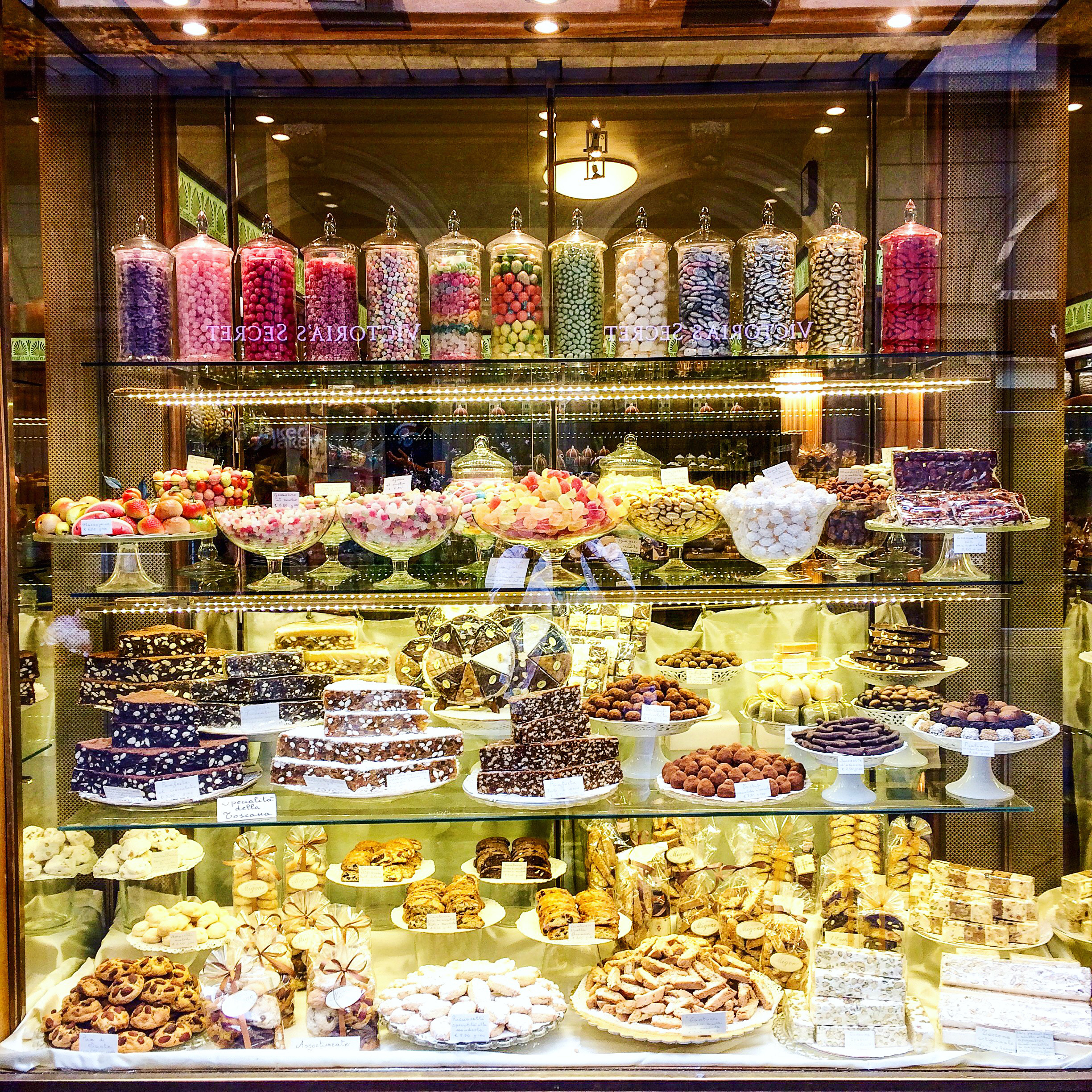 A desserts display case in a bakery with various sweets like cakes, chocolates, and candies arranged on multiple shelves and in glass jars