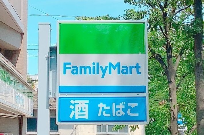 ファミリーマートの看板。「酒」「たばこ」の文字が表示されています。背景には建物や樹木が見えます。