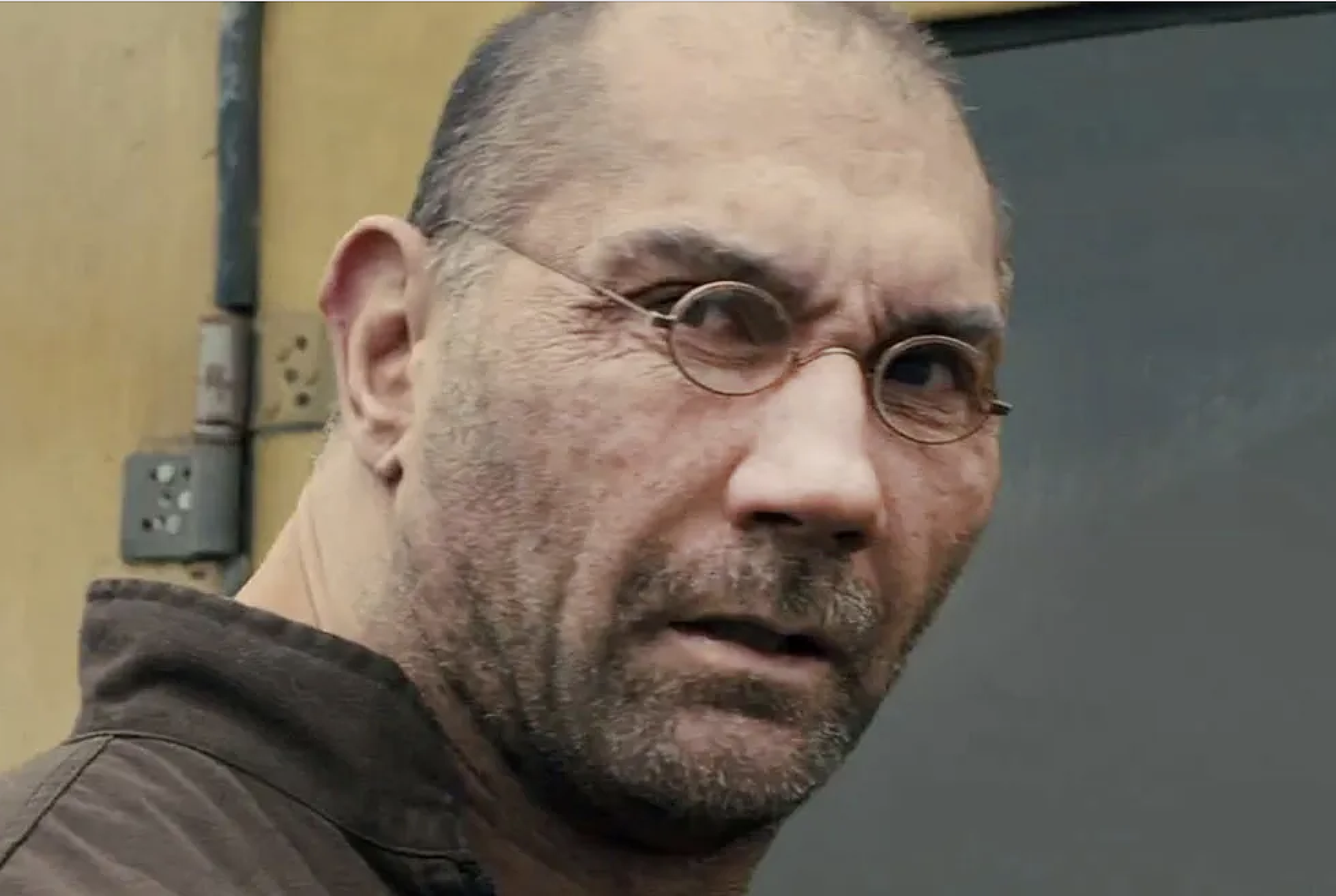 Dave Bautista wearing thin, round glasses in a serious close-up expression