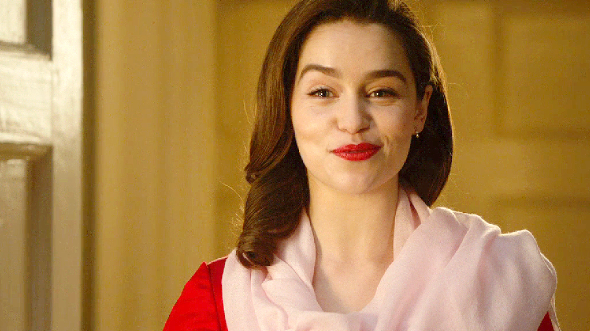 Emilia Clarke smiles, wearing a light scarf over a red outfit