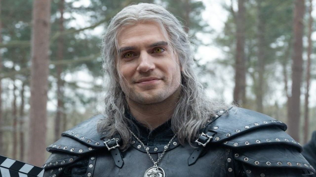 Henry Cavill dressed as Geralt of Rivia, wearing a medieval-style outfit with armor and long white hair, on set of "The Witcher."