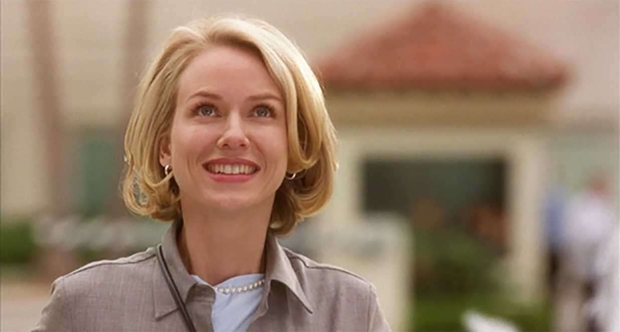 Naomi Watts smiling, looking upwards, dressed in professional attire