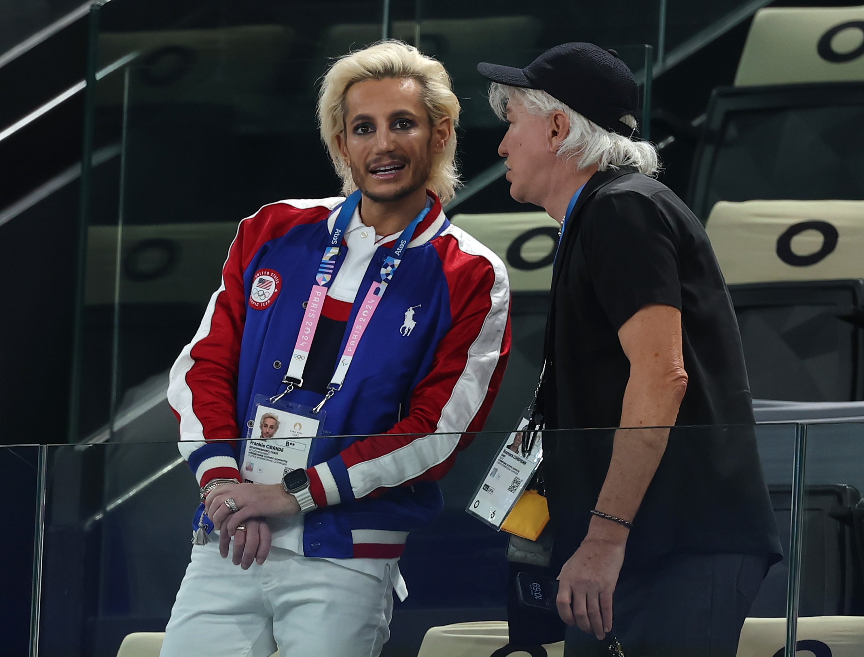 Matteo Berrettini stands in a red and blue jacket talking to coach Vincenzo Santopadre, who is wearing a black shirt and hat, at a sports event