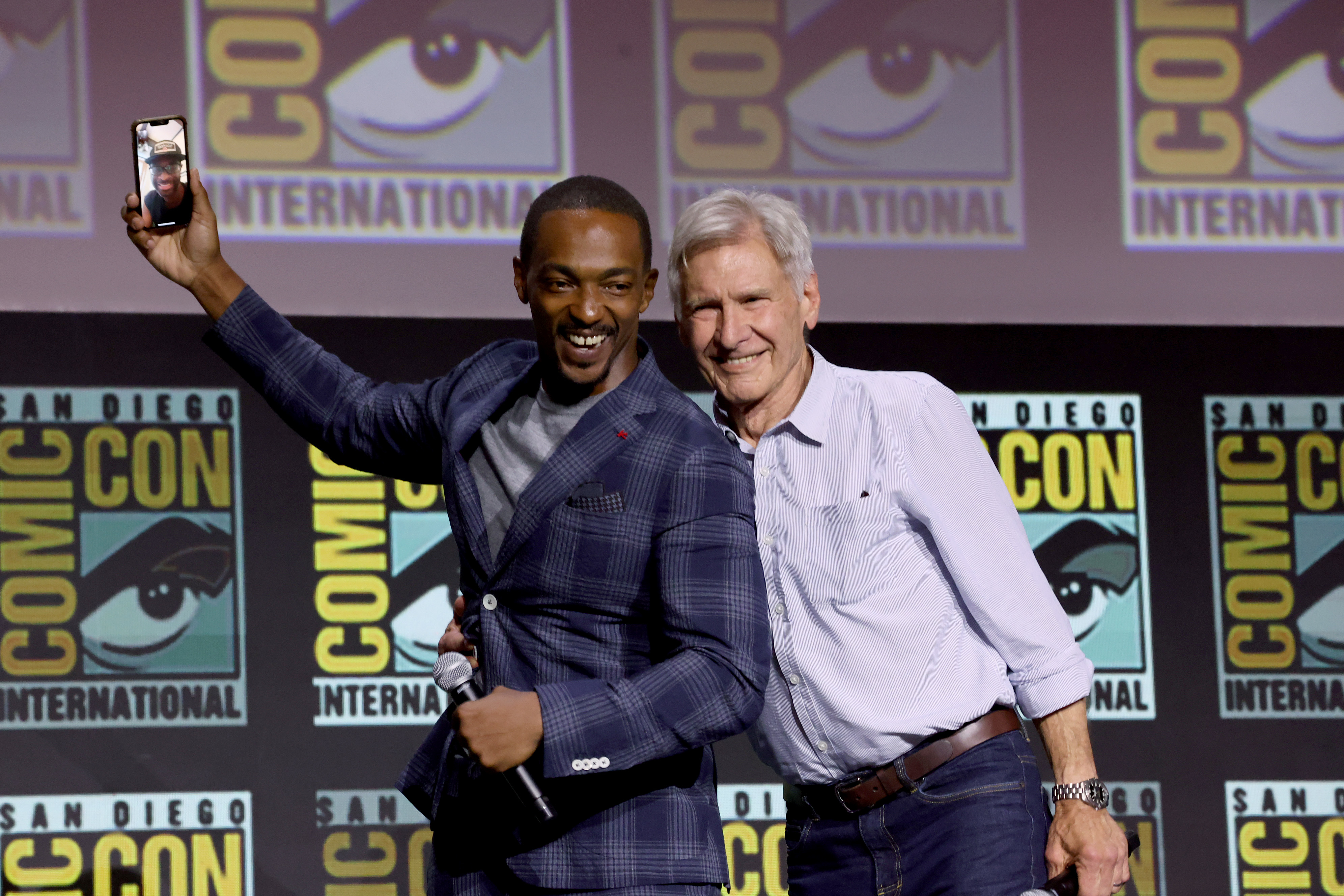 Anthony Mackie and Harrison Ford pose together on stage at San Diego Comic-Con International. Anthony takes a selfie while Harrison smiles beside him