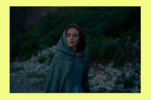 Olivia Cooke in an outdoor scene, wearing a hooded, patterned cloak, looking off to the side with a concerned expression. Rocky landscape in the background