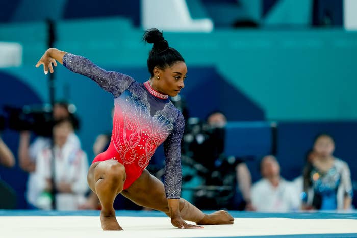 Simone Biles performs a gymnastics floor routine during a competition. Fans and photographers are visible in the background
