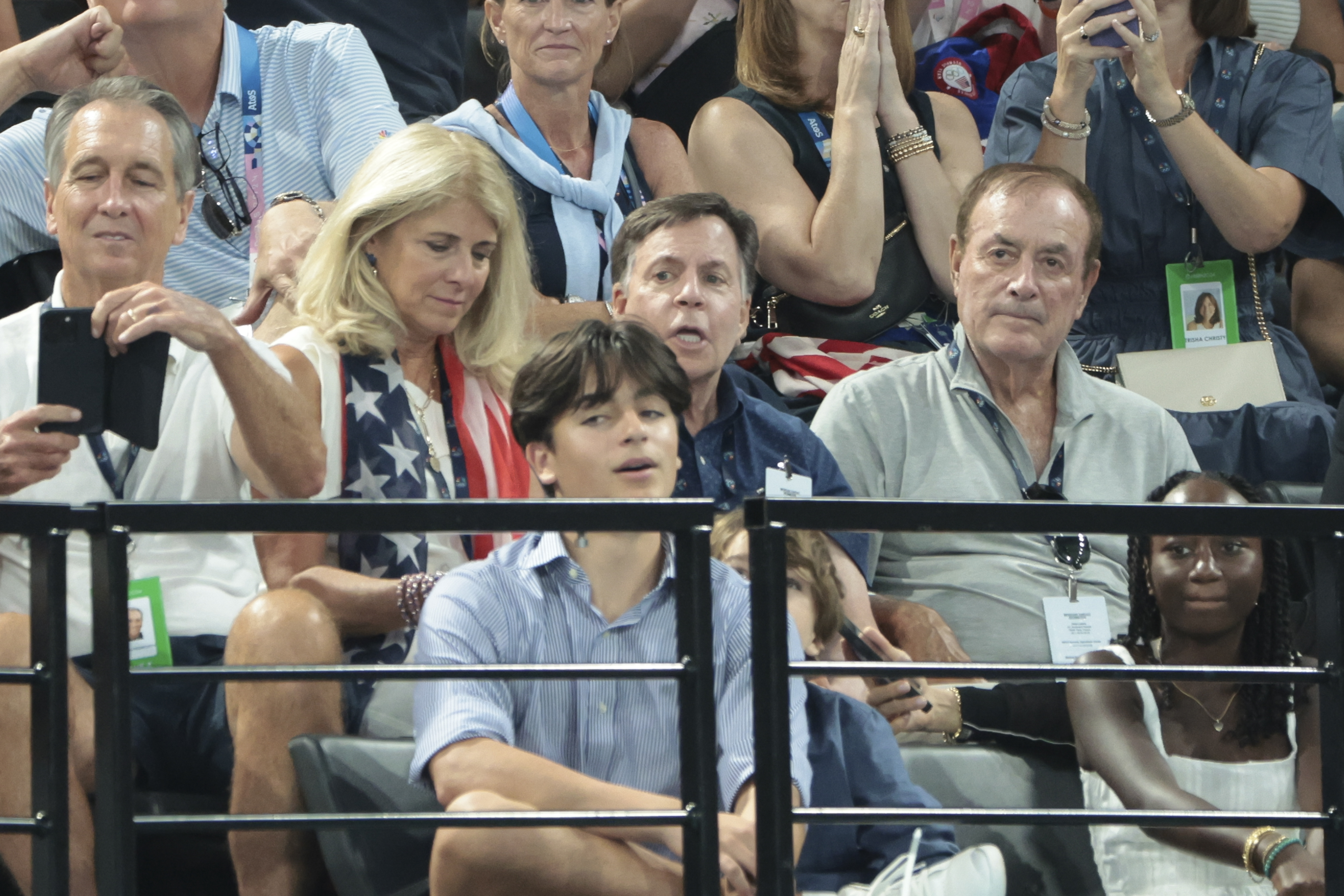 A group of people, including Bob Costas and Al Michaels, are seated in a stadium, watching an event
