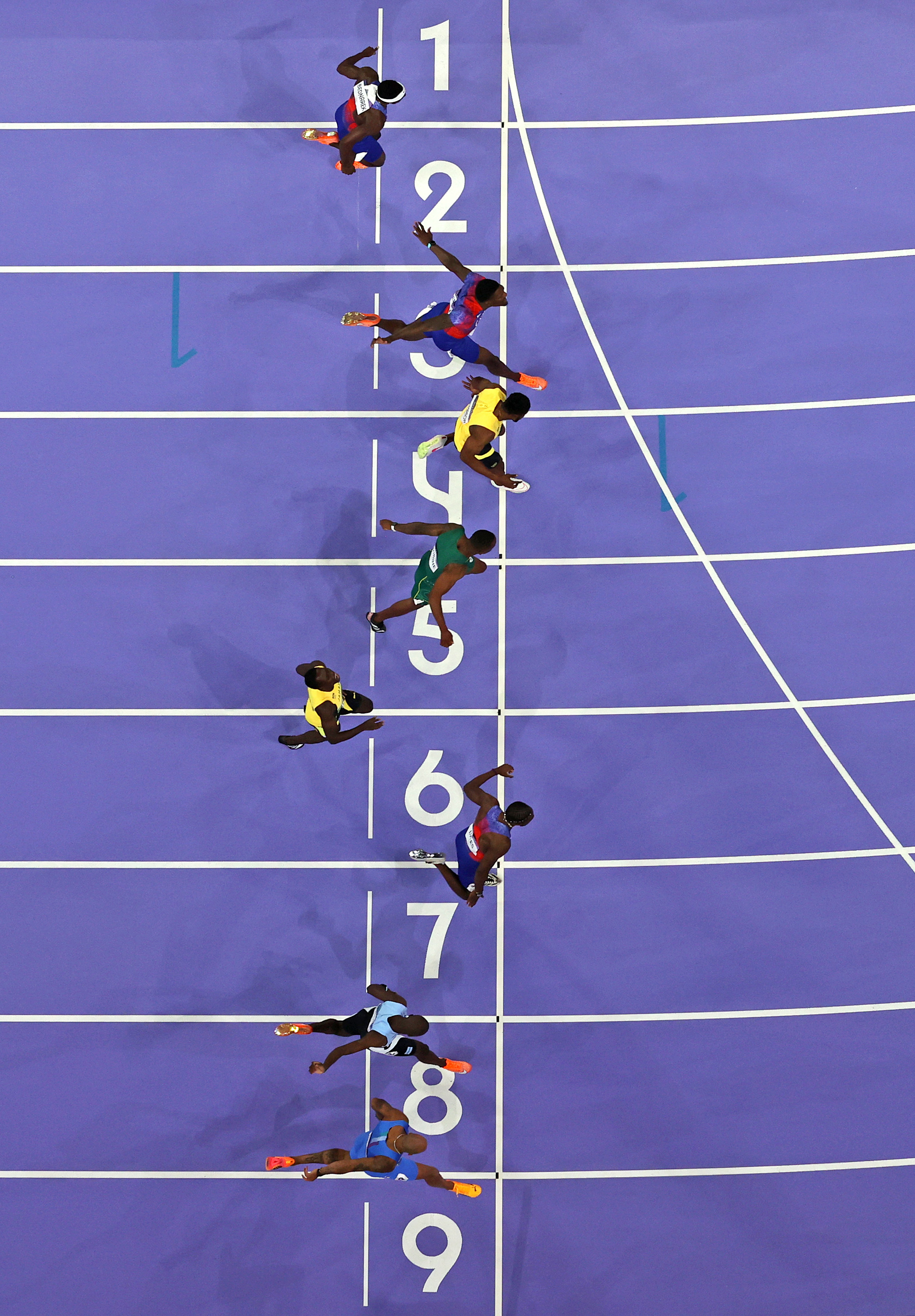 Aerial view of athletes crossing the finish line of a race, positioned on lanes 1 to 9. Names are not provided