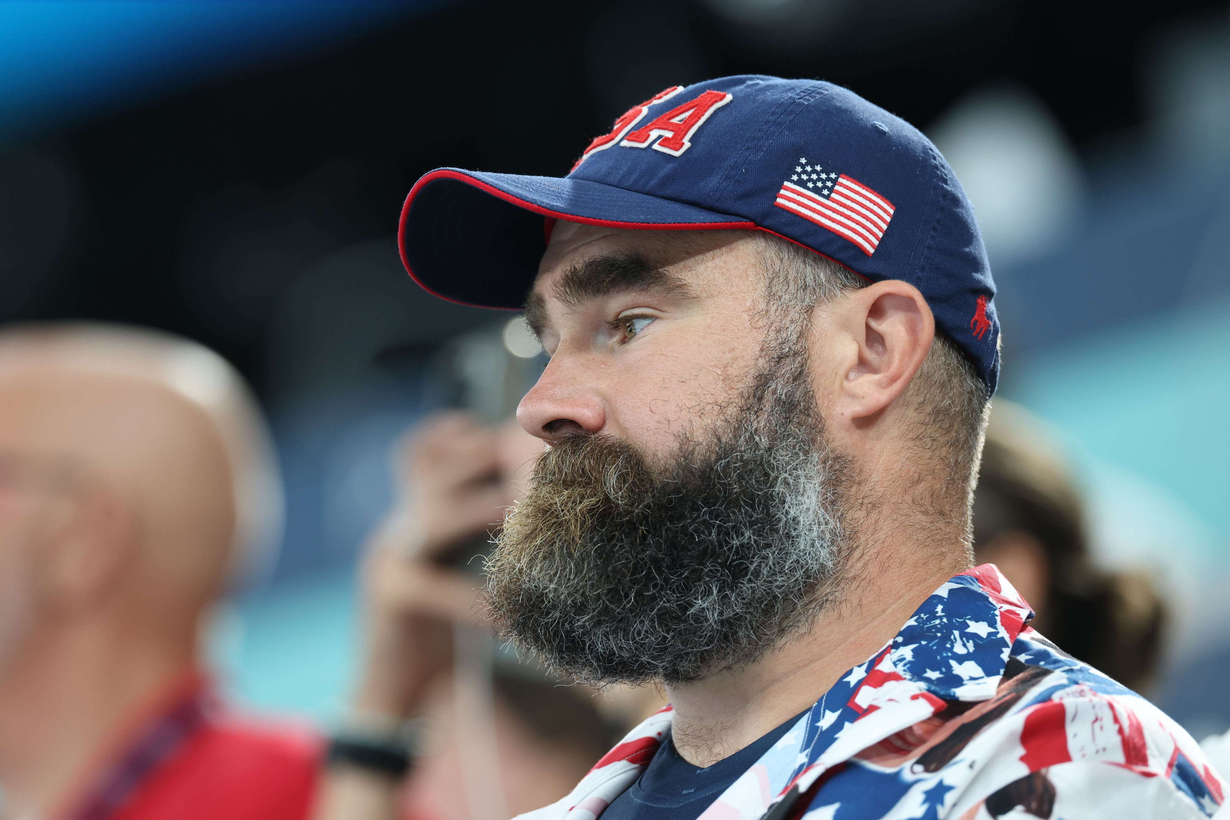 Man with a USA hat and a beard, wearing a patterned shirt with American flag design at a public event