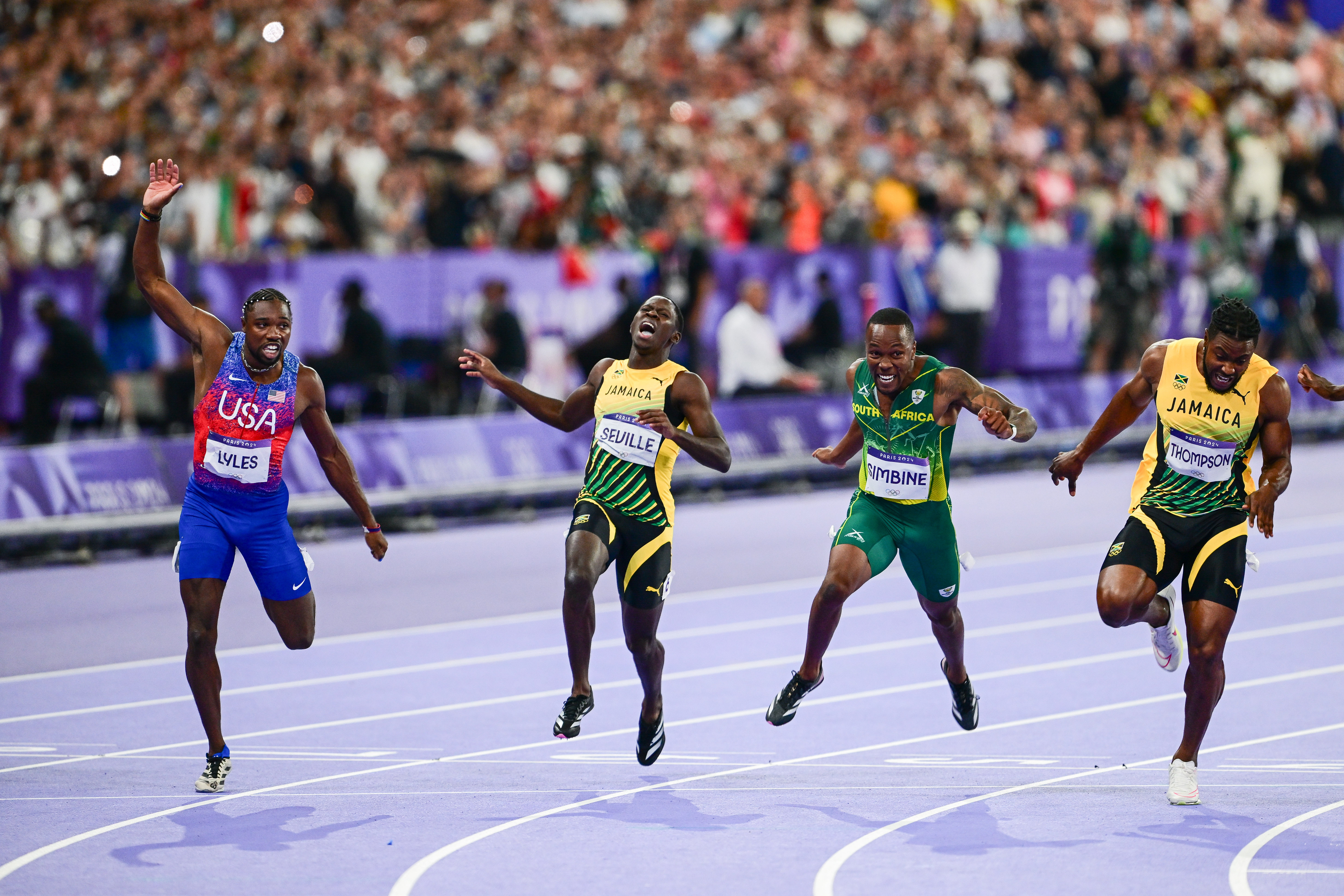 Noah Lyles, Ferdinand Omanyala, and three unidentified sprinters compete in a thrilling track race at a major event, all making a final sprint towards the finish