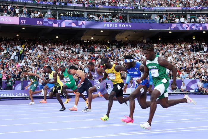 Athletes participate in a track and field race at the Paris 2024 Olympics, cheered on by a packed stadium