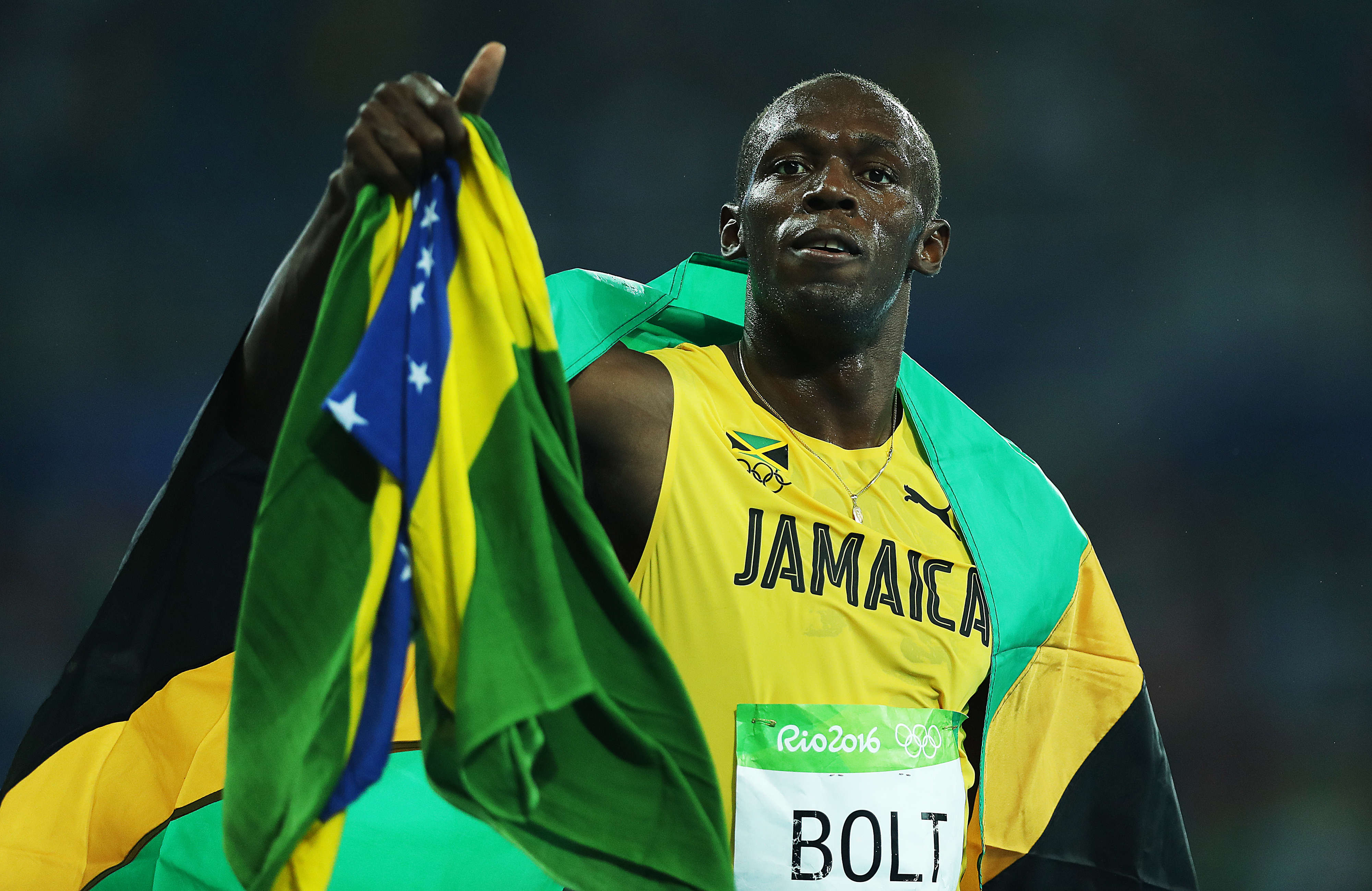 Usain Bolt, wearing a jersey with "Jamaica" on it, holding the Jamaican flag after a race at the Rio 2016 Olympics
