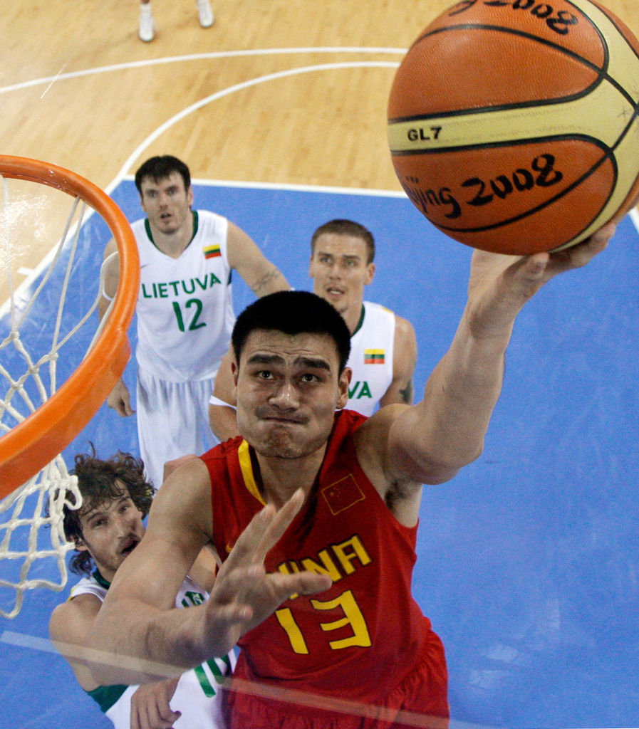 Yao Ming wearing a  jersey with number 13, leaps to make a basketball shot during the 2008 Olympics game against Lithuania. Lithuanian players in jerseys look on