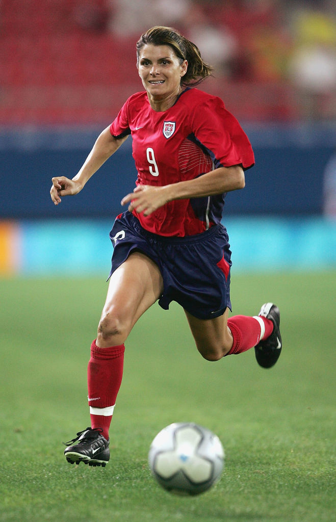 Mia Hamm in a Team USA soccer uniform dribbles a soccer ball on the field during a game