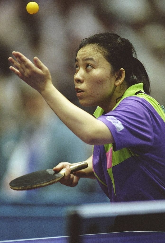 Yaping Deng preparing to serve during a match, intensively focused on the ball.