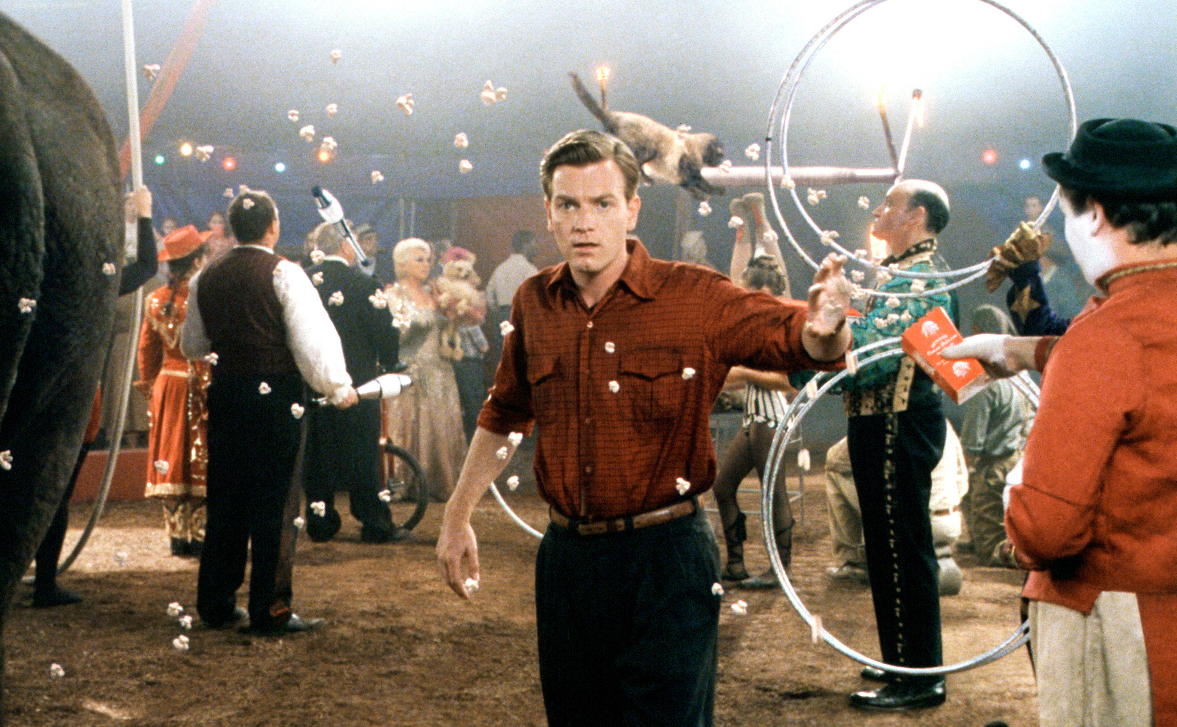 Ewan McGregor in a circus scene from a movie, background includes circus performers, an elephant, and audience members watching