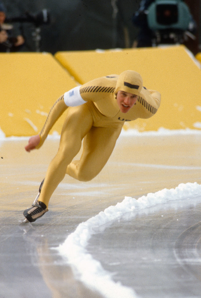 Eric wearing a fitted racing suit and helmet glides around a curve on an ice rink during a race