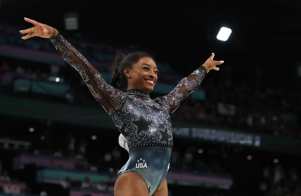 Simone Biles celebrates during a gymnastics competition, wearing a sparkly leotard with &quot;USA&quot; written on it