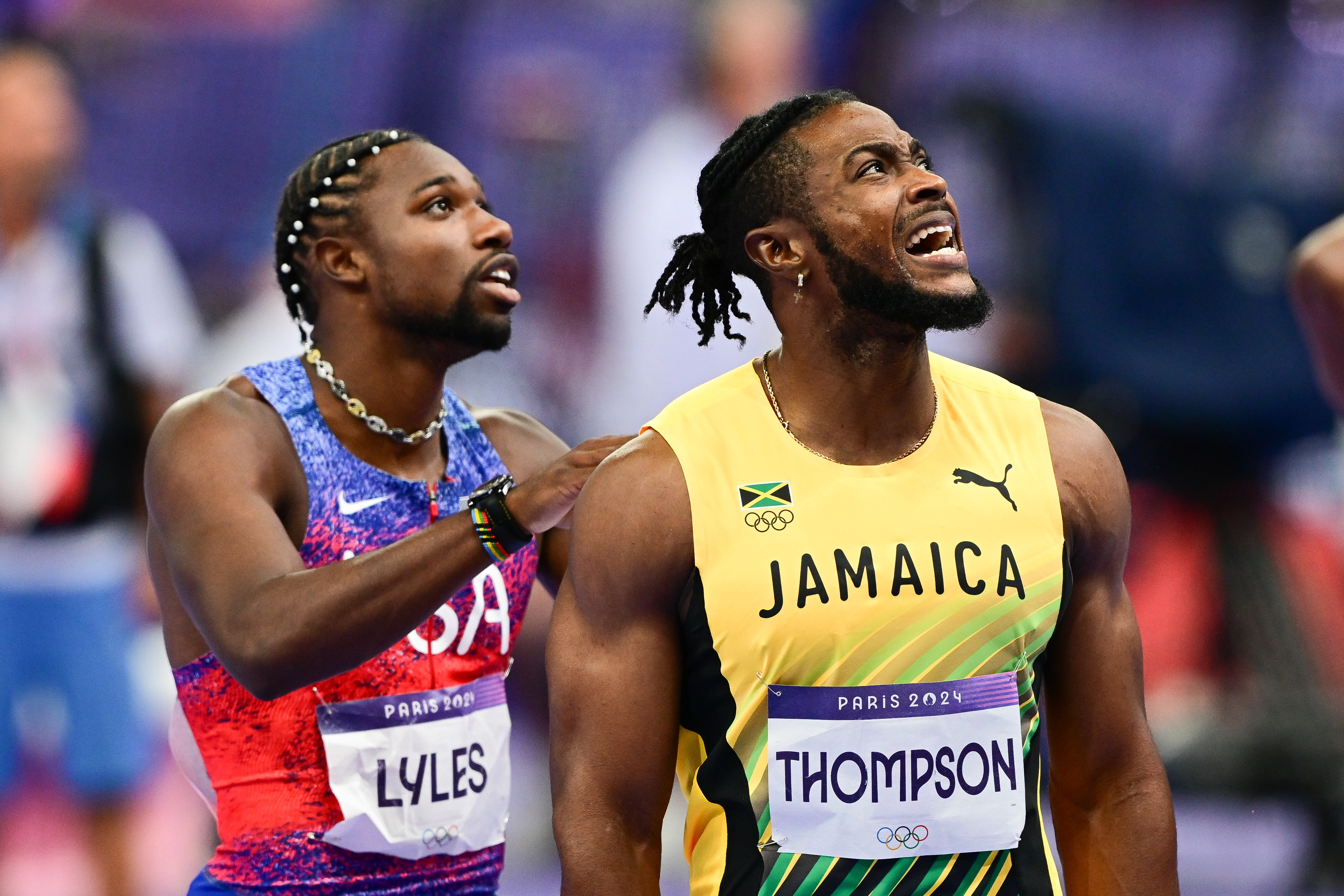 Noah Lyles in USA uniform and Andrew Hudson in Jamaica uniform standing together, looking upward during a track event