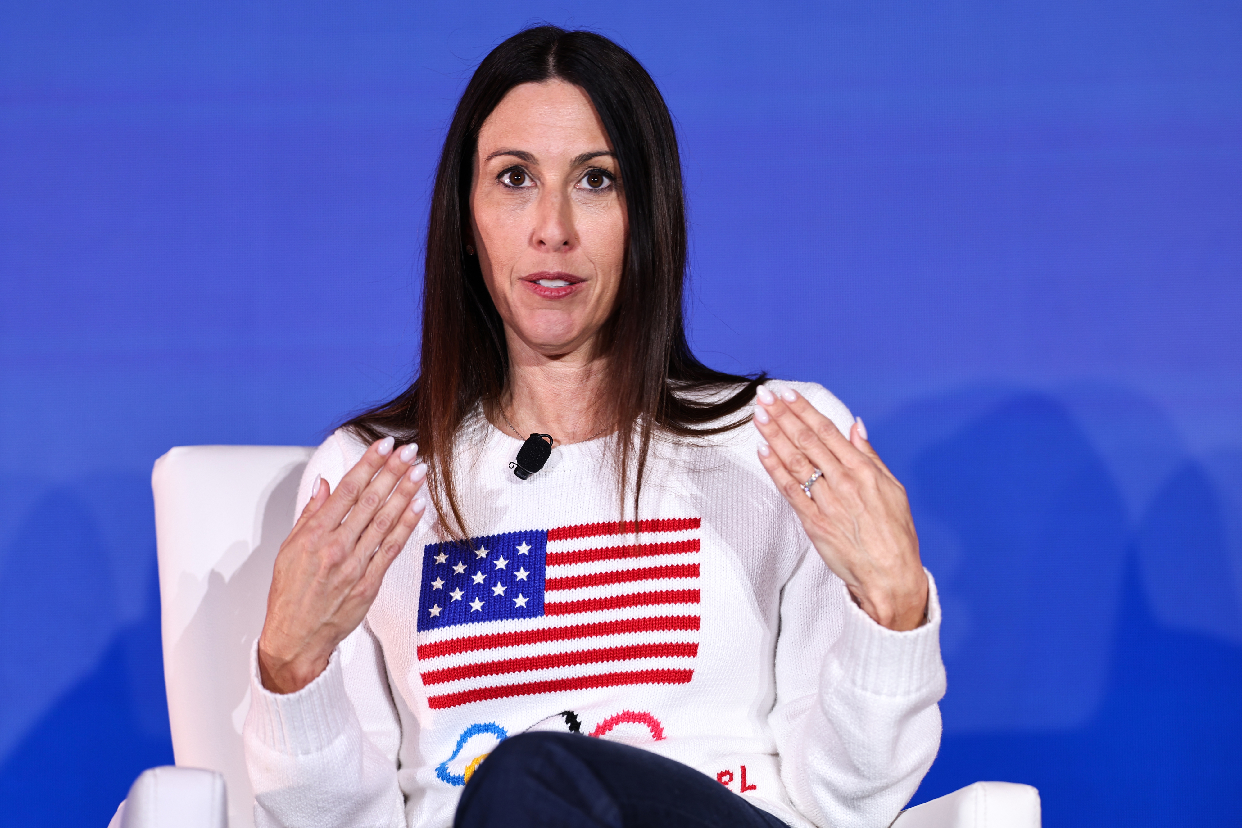 Janet Evans speaking, wearing a white sweater with an American flag and Olympic rings