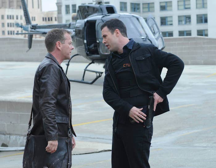 Kiefer Sutherland and Freddie Prinze Jr in tactical gear have a tense discussion on a rooftop, with a helicopter in the background