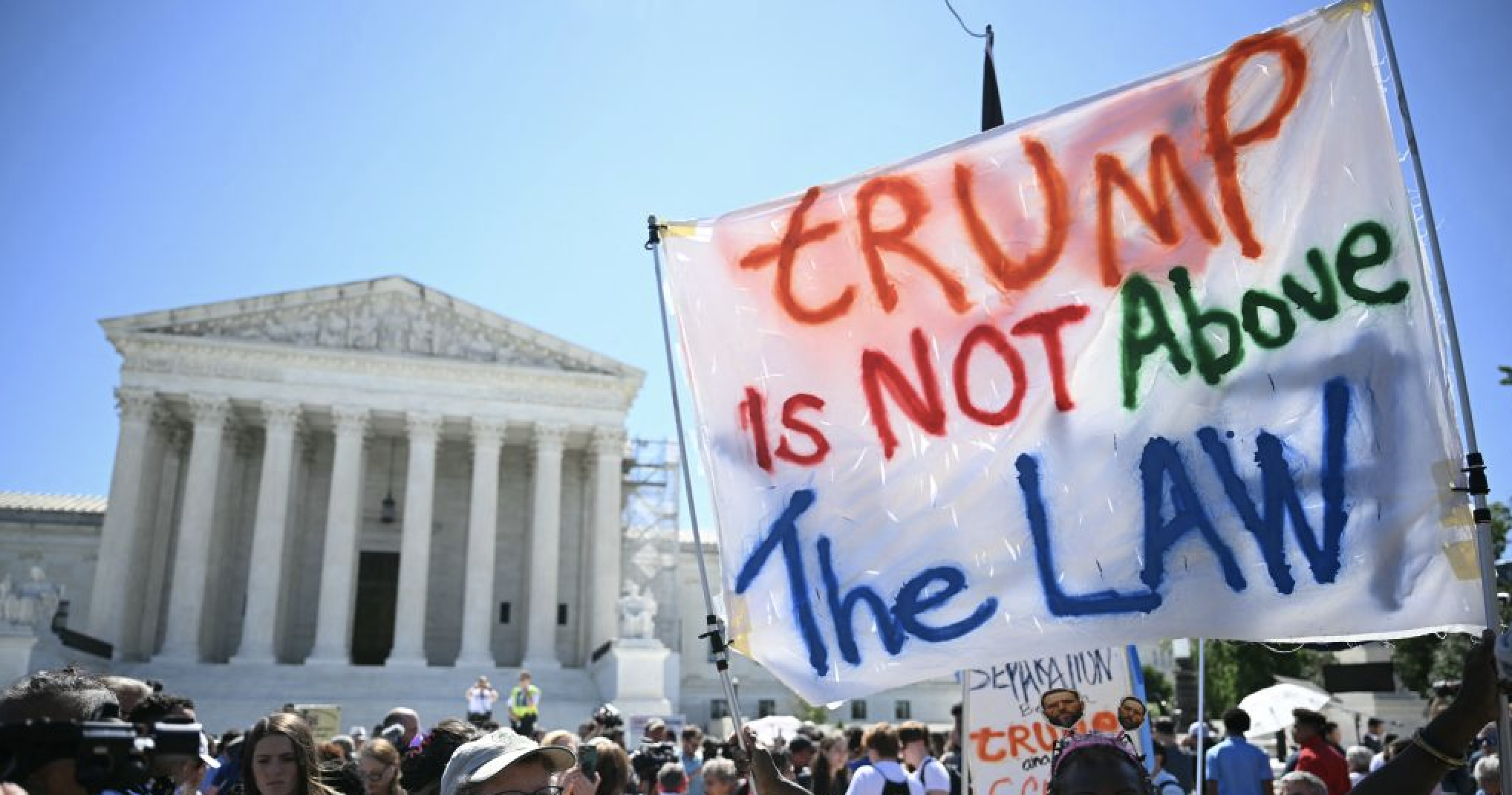 Protesters outside the U.S. Supreme Court hold a sign saying "TRUMP is NOT Above The LAW."