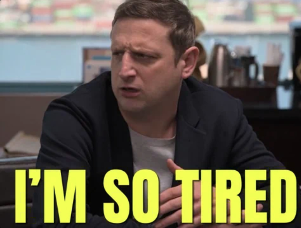 A man in a blazer with a concerned expression and the text "I'M SO TIRED" in bold yellow letters