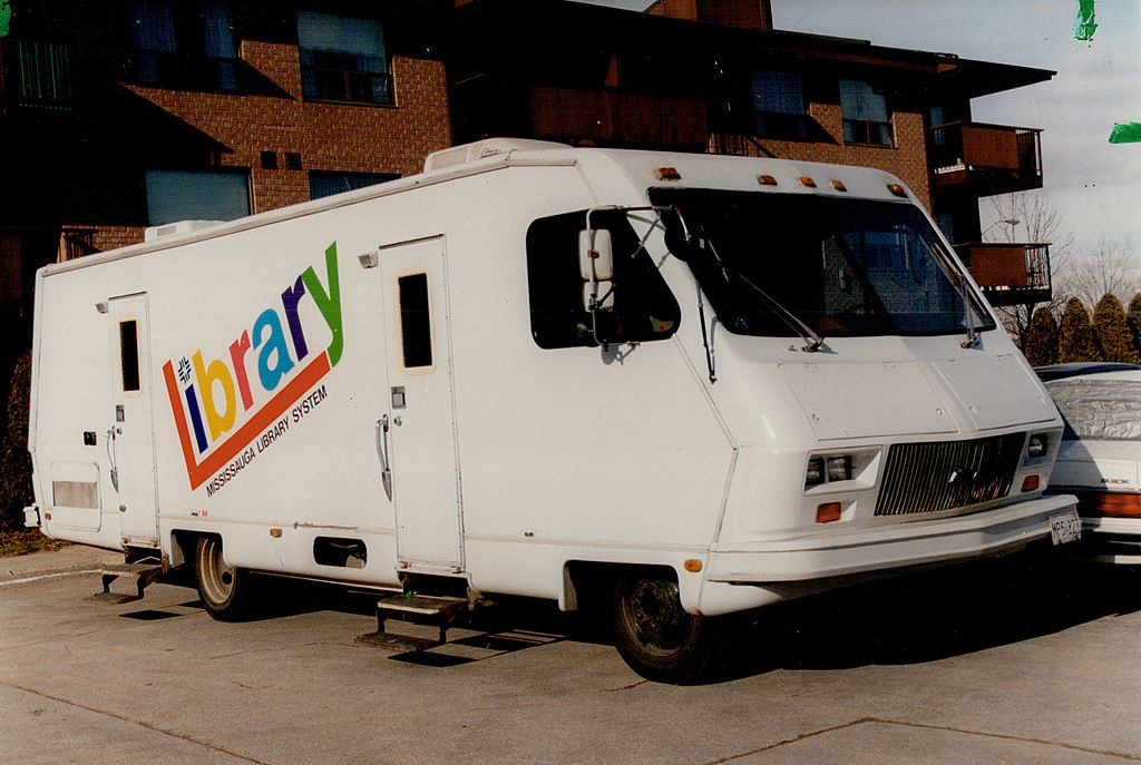 A white mobile library vehicle, part of the North York mobile library system, is parked with buildings in the background