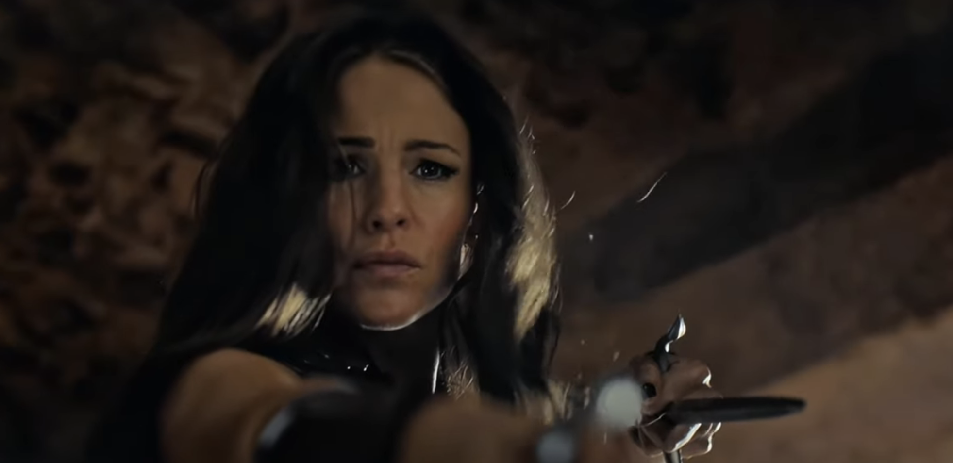 A determined woman holds a sword in a defensive stance, focusing intensely on an off-screen threat in a dramatic scene from a TV show or movie