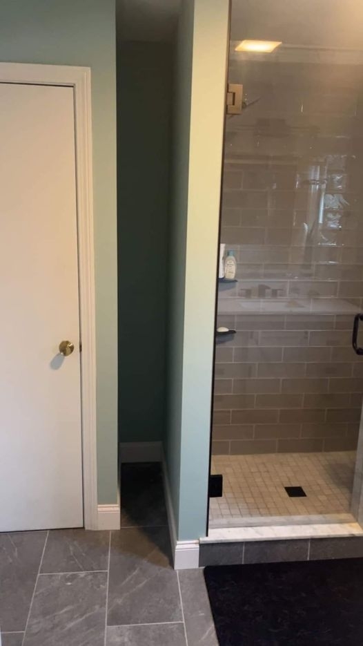 Bathroom with a glass-door shower and white-tiled interior, next to a closed white door