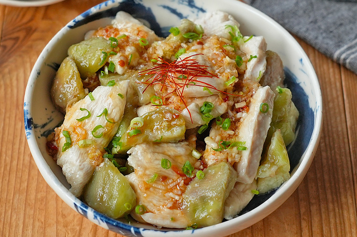 野菜と鶏肉が盛り付けられた料理が、大きな器に入れられテーブルに置かれている。背景に箸や布巾が見える。