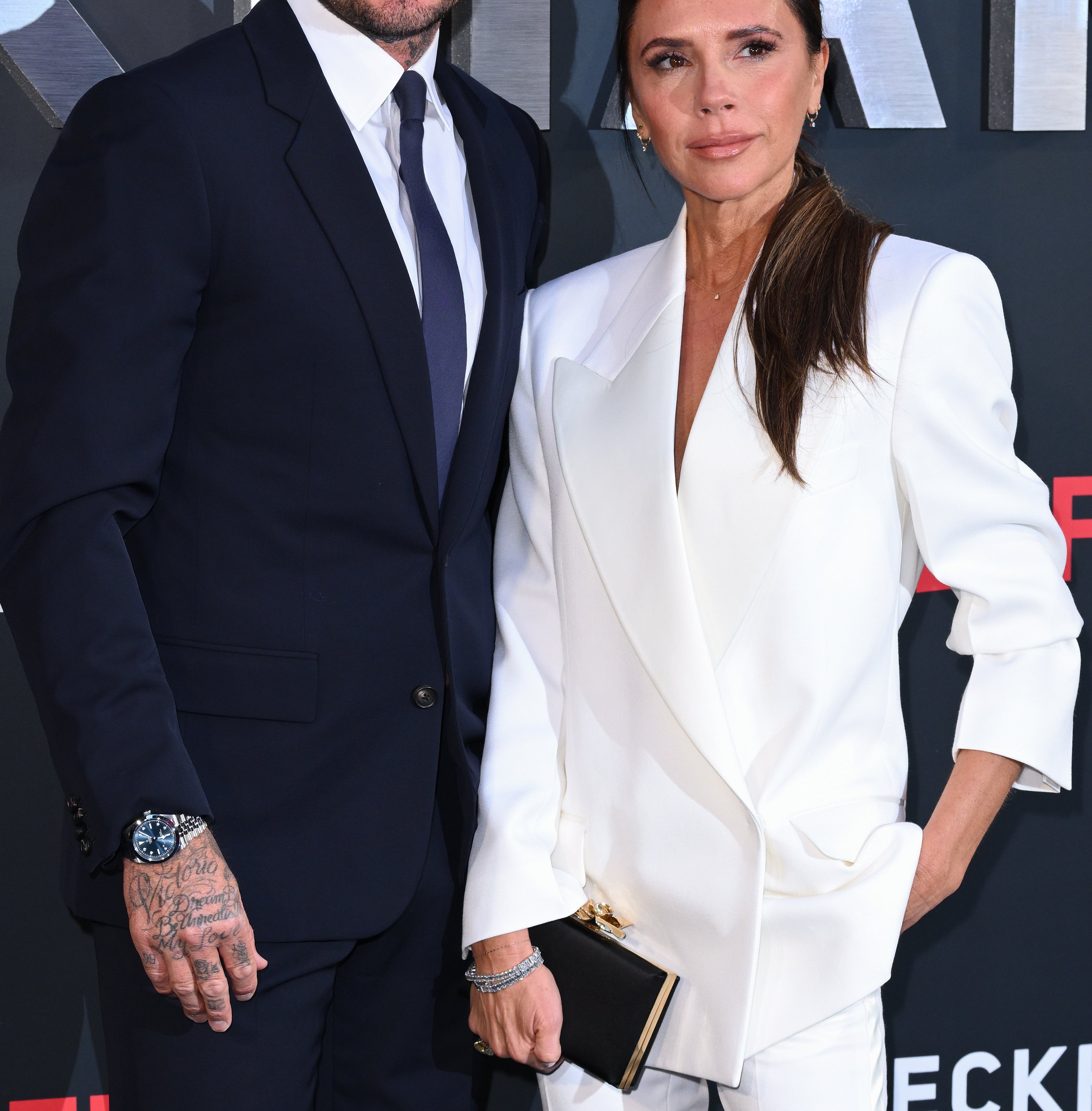 David Beckham in a dark suit and Victoria Beckham in a light suit at a Netflix event, posing together on the red carpet